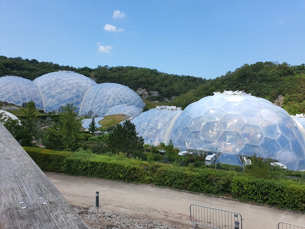 Sover Travel - A series of large, white geodesic dome structures in a lush, green landscape. The domes have a hexagonal pattern and are partially surrounded by trees and greenery, with a clear blue sky overhead.