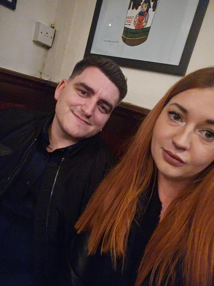 Sover Travel - A man named Jake and a woman, both with red hair, are sitting together in a room. Jake is on the left, smiling warmly, while the woman looks at the camera with a neutral expression. It’s October 2024, and framed artwork adorns the cream wall behind them.