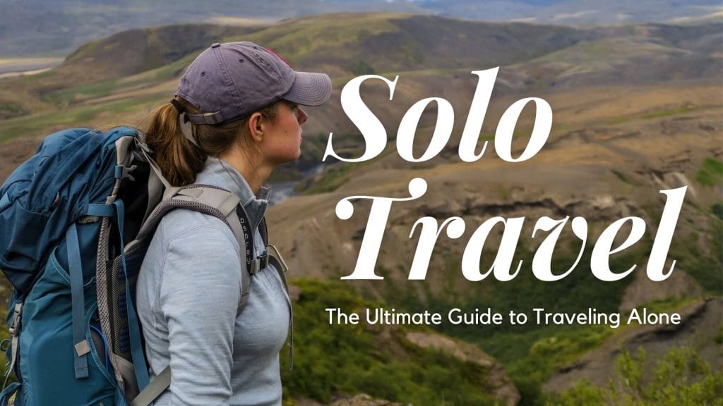 Sover Travel - A person with a backpack gazes at a vast, mountainous landscape. The words Solo Travel: The Ultimate Guide to Traveling Alone appear on the image. With journey confidence and wearing a cap and outdoor gear, they embrace the adventure ahead.