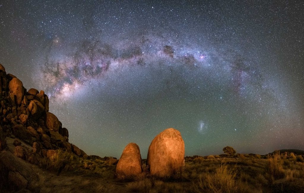 **Alt Text:** A stunning view of the Milky Way arching over rocky terrain under a starry night sky. **Caption:** Experience the serenity of stargazing in nature, perfect for mindful travel and wellness retreats. **Image Description:** A panoramic view of the Milky Way above rocky formations in a tranquil landscape.