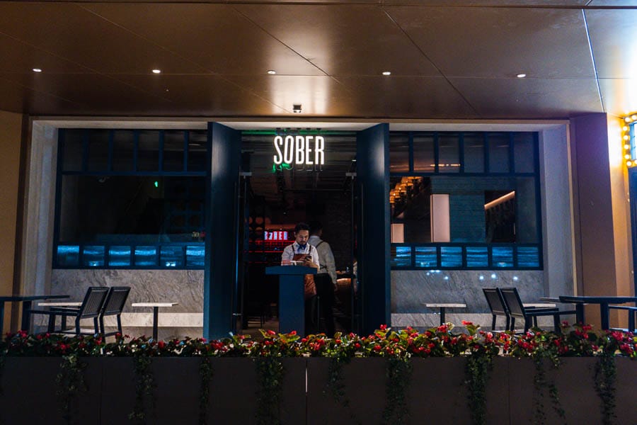 **Alt Text:** Entrance of a restaurant named "SOBER" with a staff member at the door. **Caption:** Discover mindful dining at "SOBER," where wellness meets culinary delight. **Image Description:** A restaurant entrance featuring the name "SOBER" and a staff member welcoming guests.